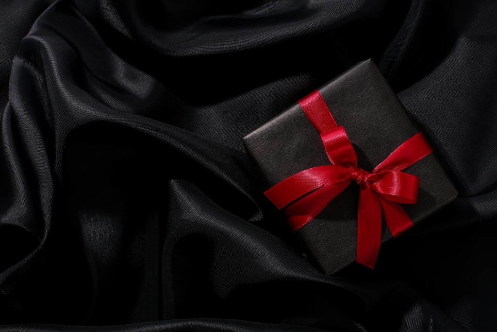 black gift box with red ribbon on a black satin textile